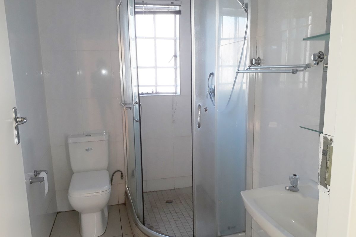 A functional bathroom featuring a corner shower enclosure, white toilet, wall-mounted washbasin, and tiled finishes throughout.