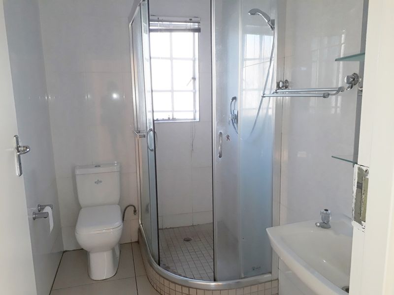A functional bathroom featuring a corner shower enclosure, white toilet, wall-mounted washbasin, and tiled finishes throughout.
