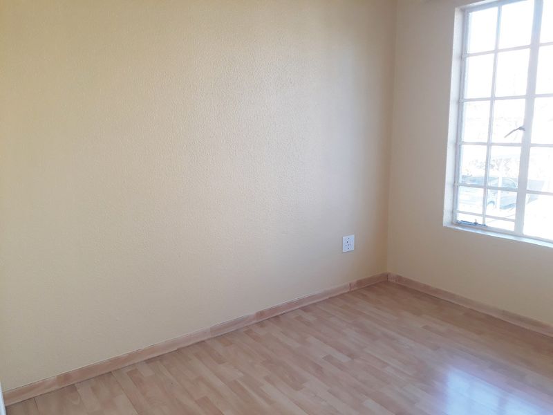 A bright, empty bedroom featuring light-toned laminate flooring, neutral walls, and a classic lattice-style window.