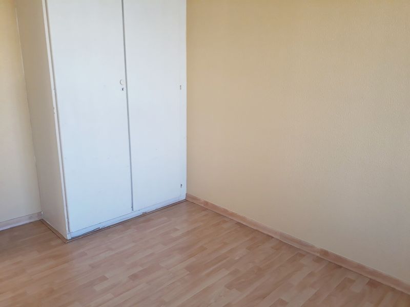 A simple, empty bedroom featuring light-toned laminate flooring and a built-in wardrobe with white doors.