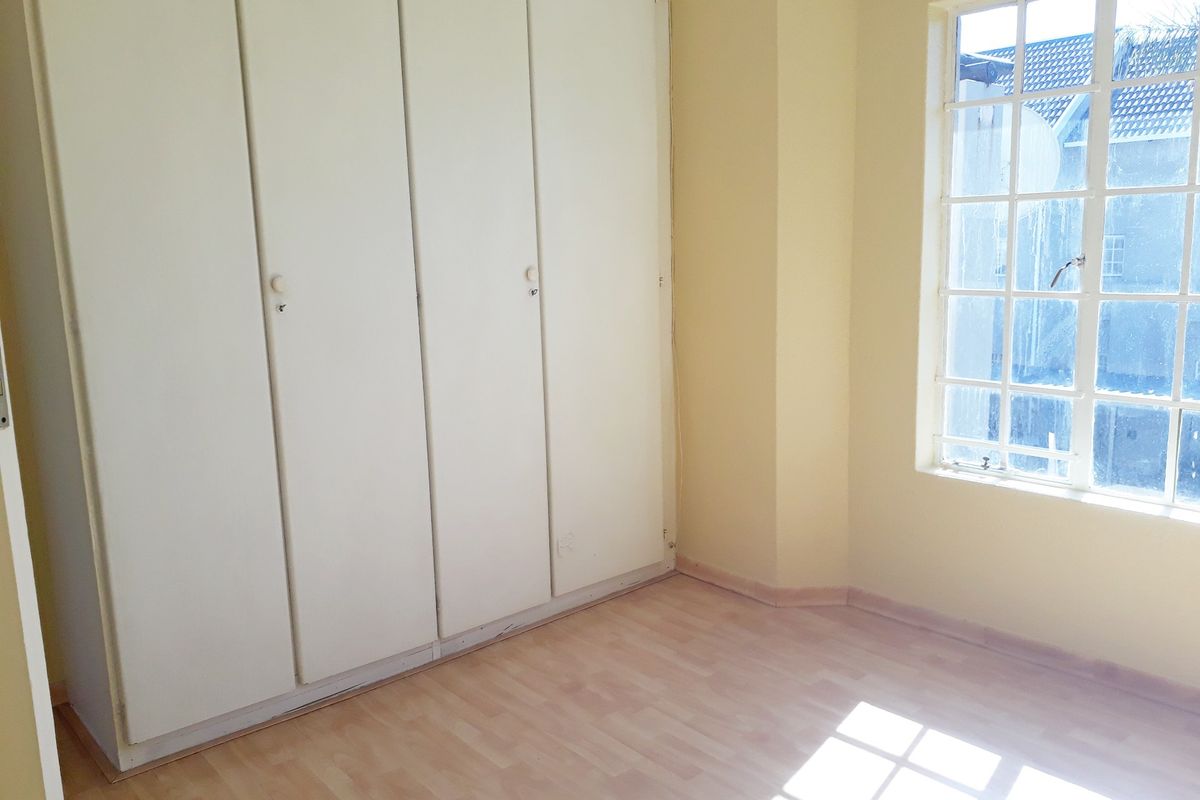 An empty bedroom featuring built-in cupboards, laminate flooring, and a large grid-style window allowing natural light.