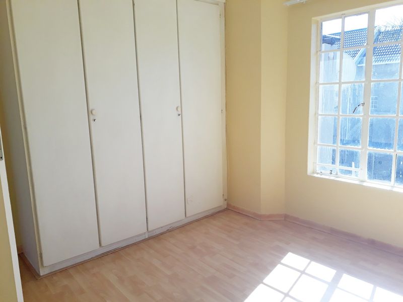 An empty bedroom featuring built-in cupboards, laminate flooring, and a large grid-style window allowing natural light.