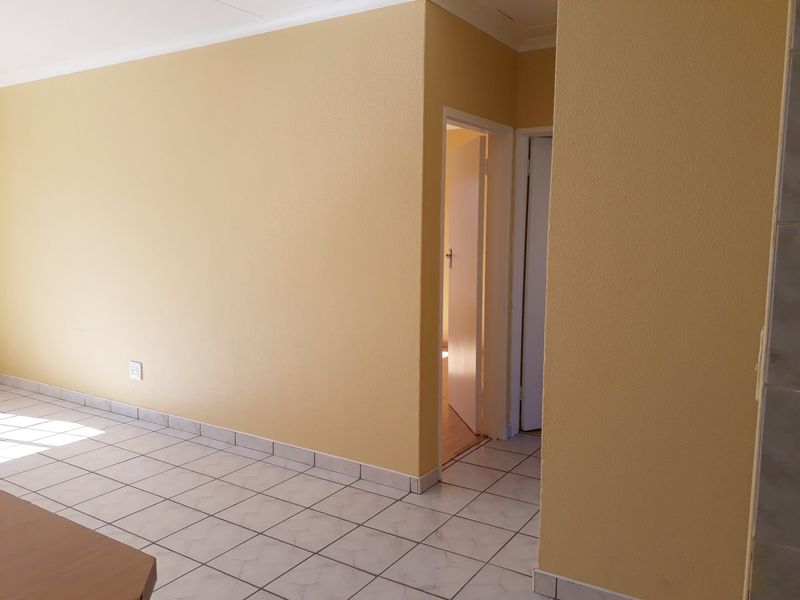 A clean, empty hallway featuring neutral yellow walls and light-colored ceramic floor tiles, providing access to adjacent rooms.