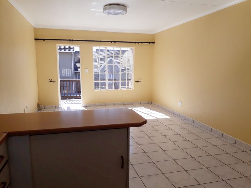 An empty open-plan living area featuring tiled flooring, neutral walls, and direct access to a small balcony through a glass-paneled door.