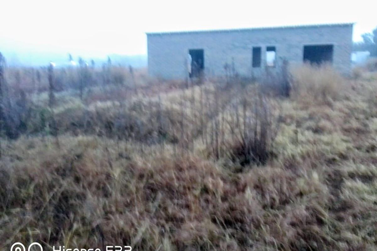A view of an unfinished masonry structure situated on a large, overgrown vacant residential plot.
