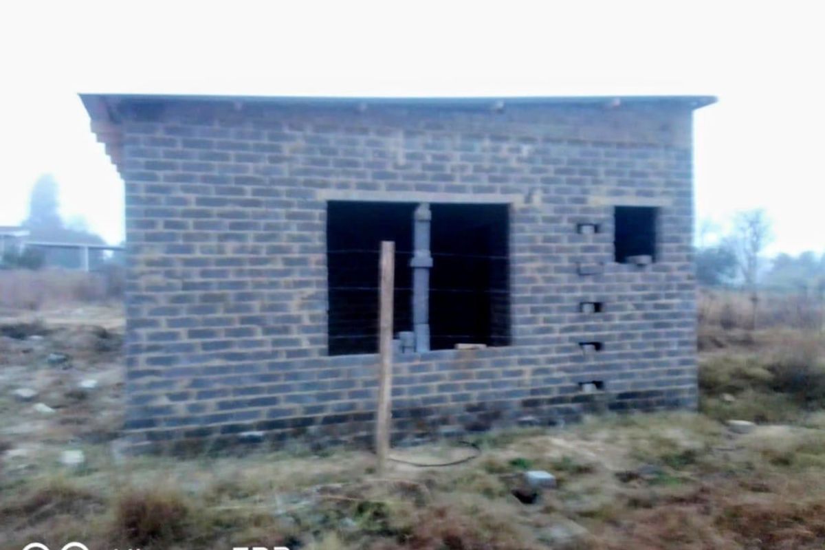 An unfinished residential structure featuring exposed brickwork and open window frames, situated on a vacant plot of land.