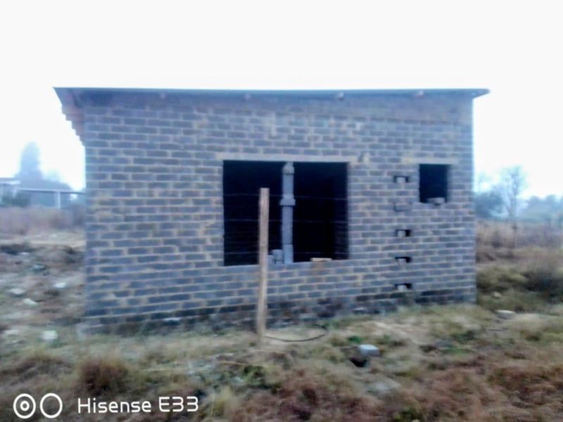An unfinished residential structure featuring exposed brickwork and open window frames, situated on a vacant plot of land.