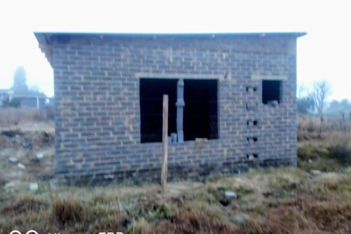 An unfinished residential structure featuring exposed brickwork and open window frames, situated on a vacant plot of land.