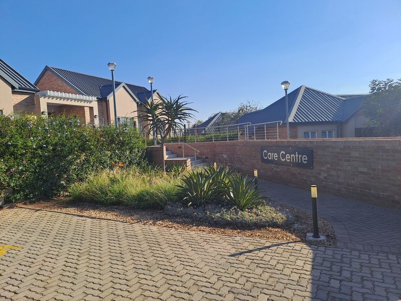 Front exterior view of the care centre facility featuring a brick retaining wall, paved driveway, and well-maintained landscaped garden area.