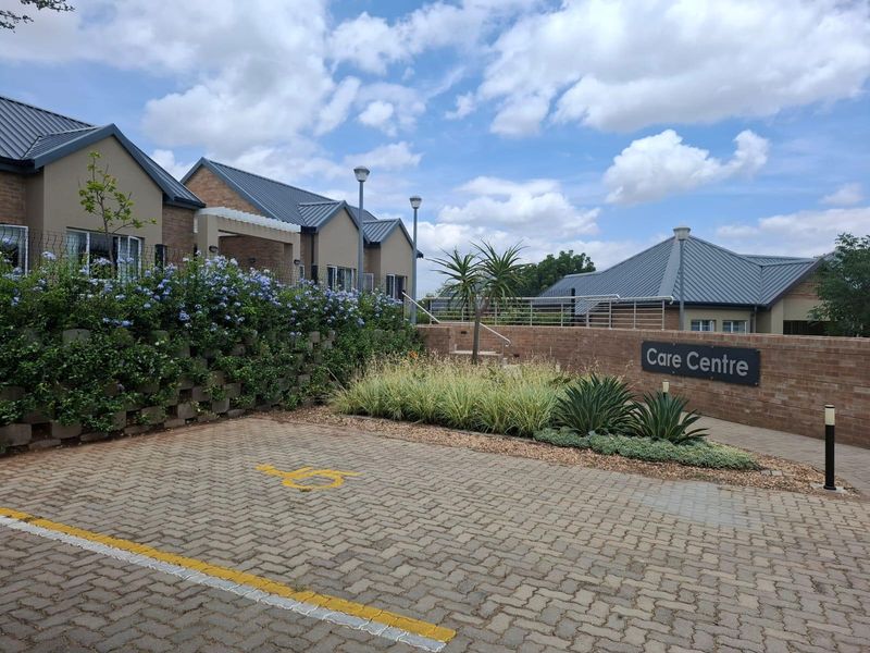 Exterior view of the residential care centre featuring a paved parking area, landscaped gardens, and well-maintained brick facade.