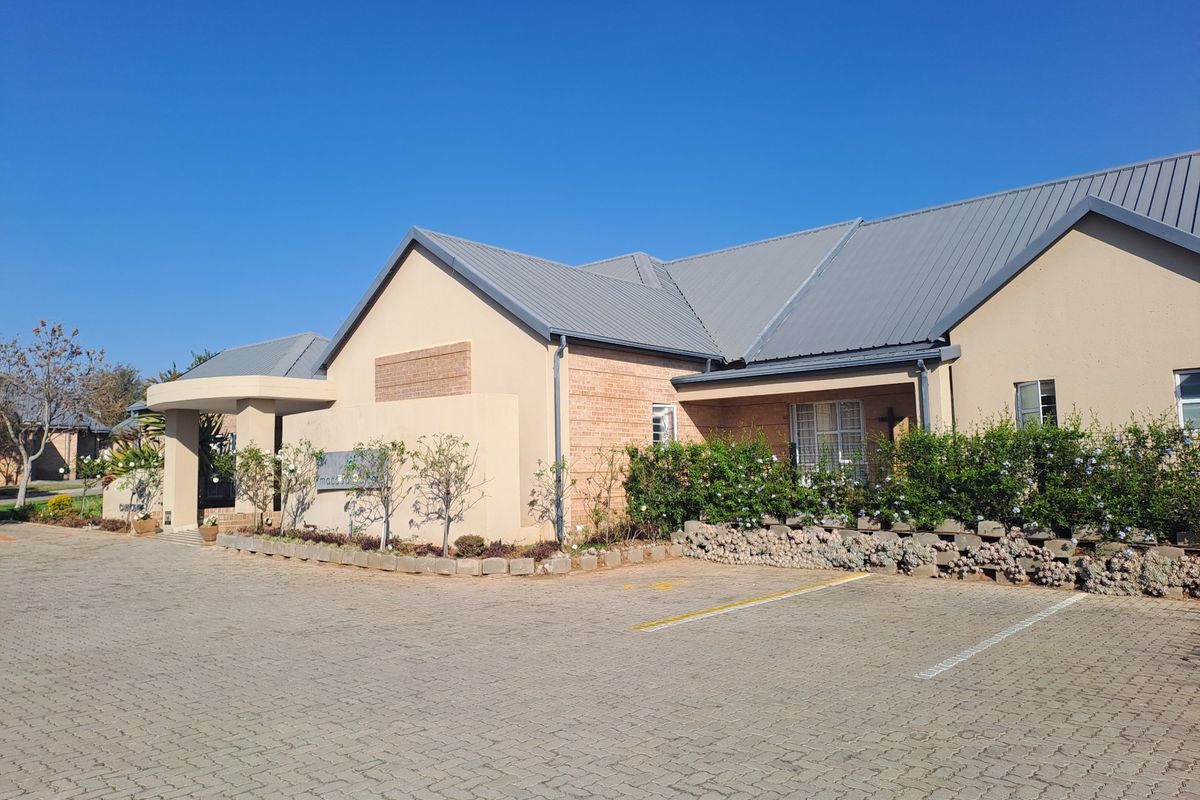 Front exterior view of a residential building featuring a metal roof, brick facade, and a paved driveway with landscaped garden borders.