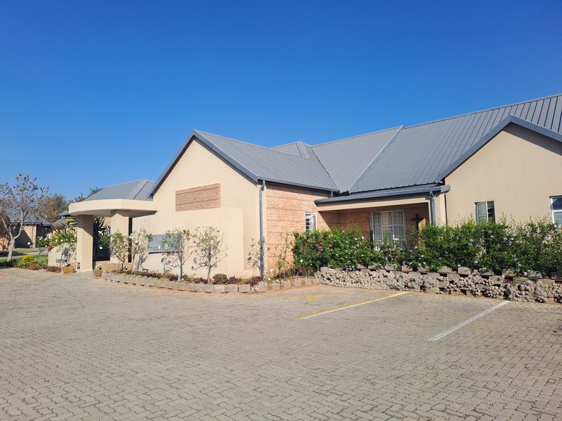 Front exterior view of a residential building featuring a metal roof, brick facade, and a paved driveway with landscaped garden borders.