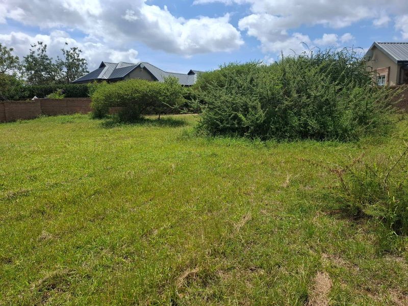 A vacant residential plot featuring a grassed area, established shrubs, and a perimeter brick wall boundary.