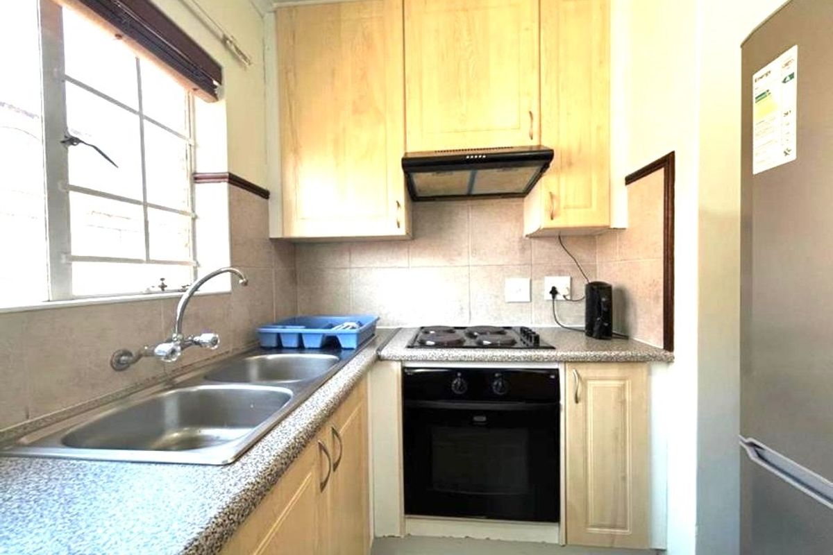 Compact kitchen featuring light wood-finish cabinetry, granite-look countertops, a built-in oven, electric hob, and a stainless steel double sink with tiled backsplash.