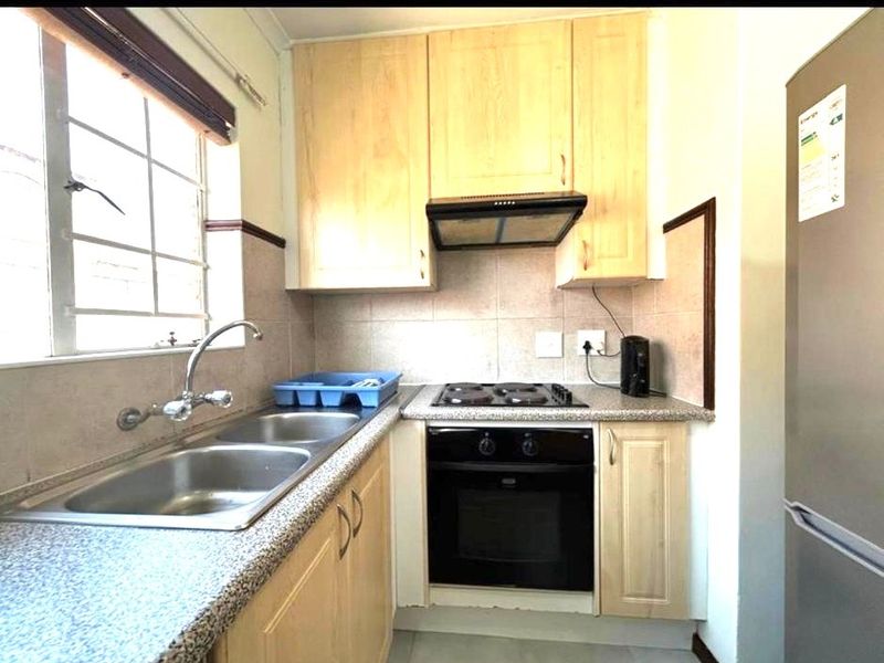 Compact kitchen featuring light wood-finish cabinetry, granite-look countertops, a built-in oven, electric hob, and a stainless steel double sink with tiled backsplash.