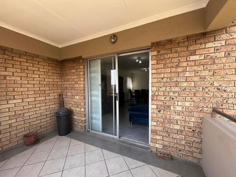 A covered balcony featuring exposed brick walls and tiled flooring, providing direct access to the interior living space through a sliding glass door.