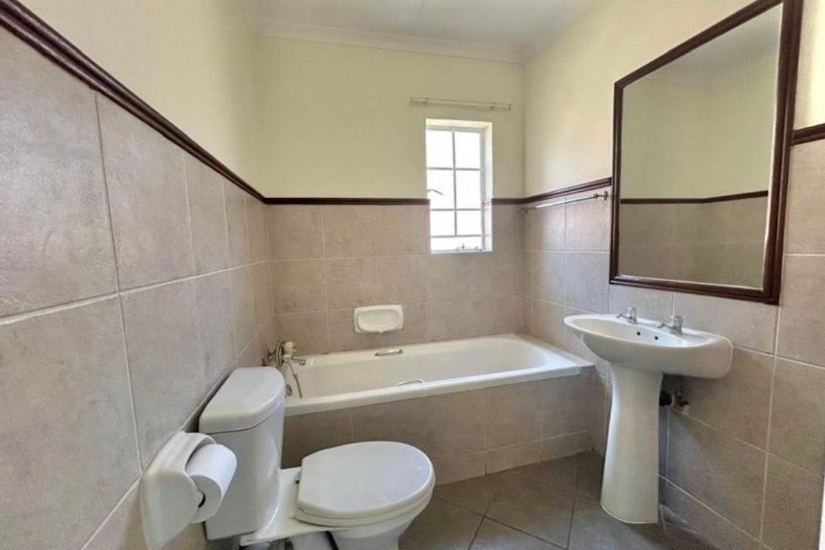 A functional bathroom featuring a pedestal washbasin, built-in bathtub, and toilet with neutral ceramic wall and floor tiling.