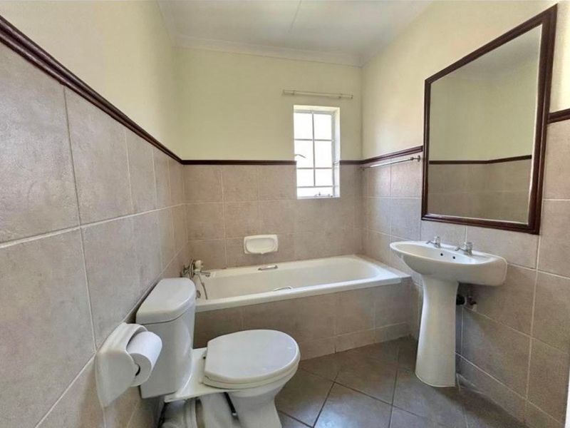 A functional bathroom featuring a pedestal washbasin, built-in bathtub, and toilet with neutral ceramic wall and floor tiling.