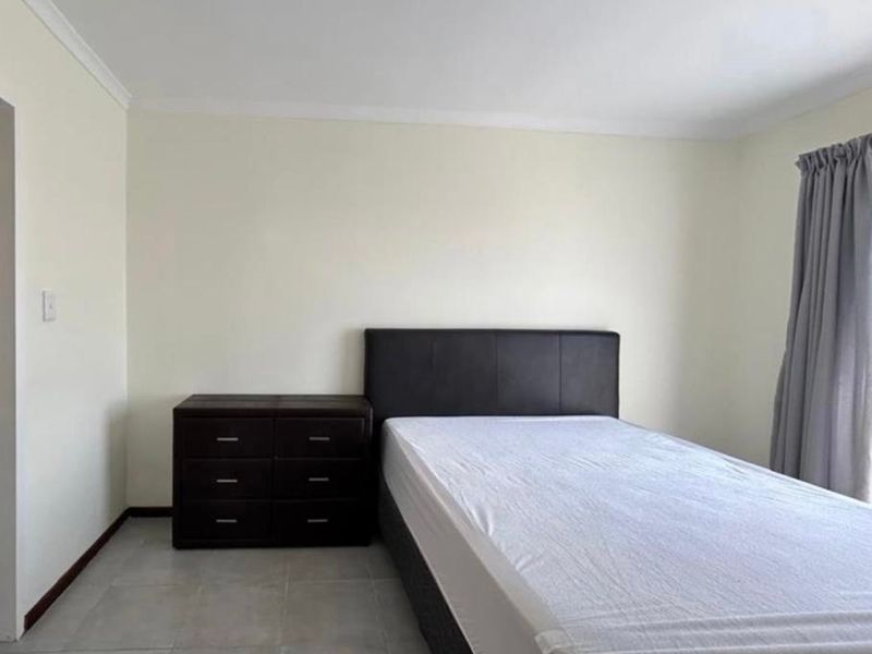 A simple bedroom featuring neutral walls, tiled flooring, and a ceiling light fixture, providing a clean and functional living space.