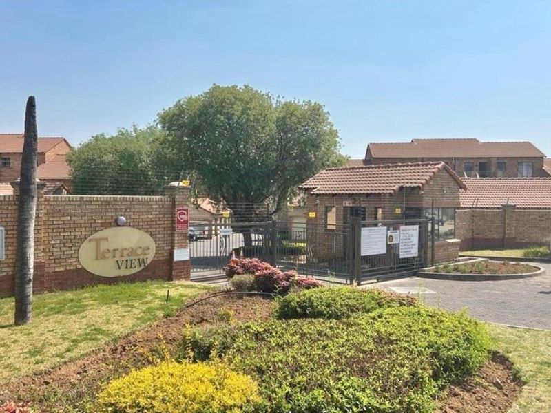 The entrance to Terrace View complex featuring a brick boundary wall, security gate, and guard house with paved driveway access.
