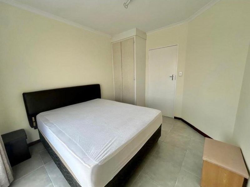 A functional bedroom featuring tiled flooring, a built-in wardrobe, and neutral wall finishes.