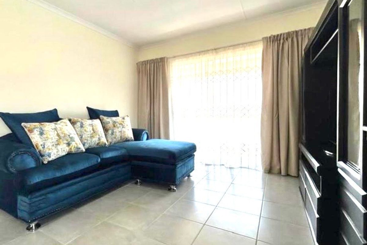 A living room featuring neutral tiled flooring, a ceiling light fixture, and large windows with curtain tracks, offering a functional and well-lit space.
