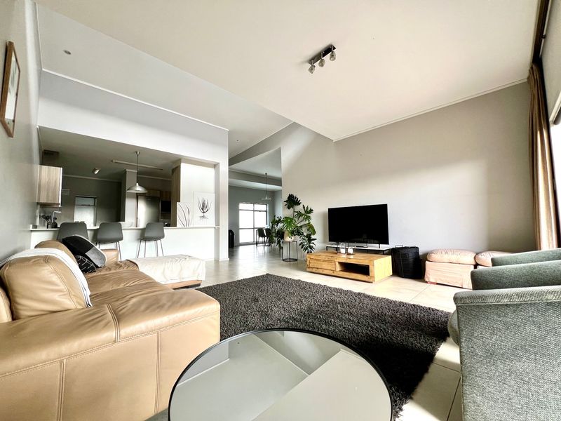 Spacious open-plan living area featuring a modern kitchen with a breakfast bar, neutral tiled flooring, and recessed lighting throughout the connected living space.