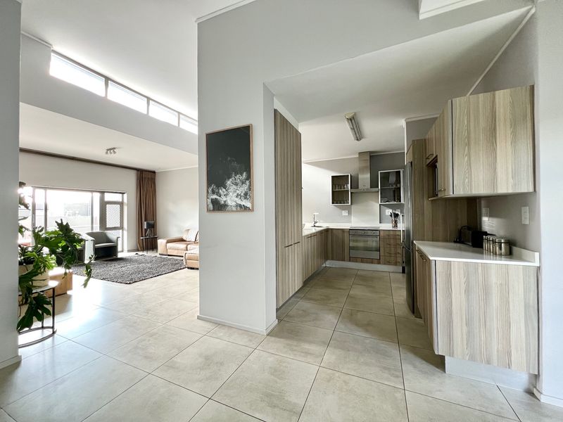 Spacious open-plan living area featuring a modern kitchen with wood-finish cabinetry, integrated appliances, and large windows providing ample natural light.