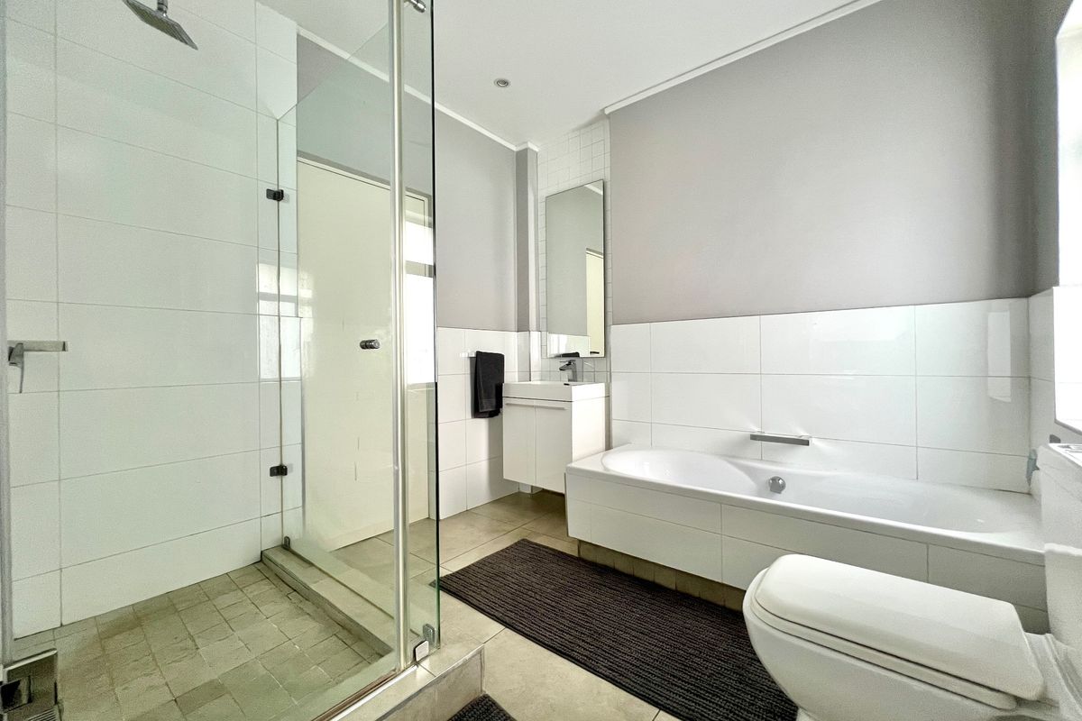 Modern bathroom featuring a walk-in shower with glass screen, built-in bathtub, wall-mounted vanity, and neutral tiled finishes.