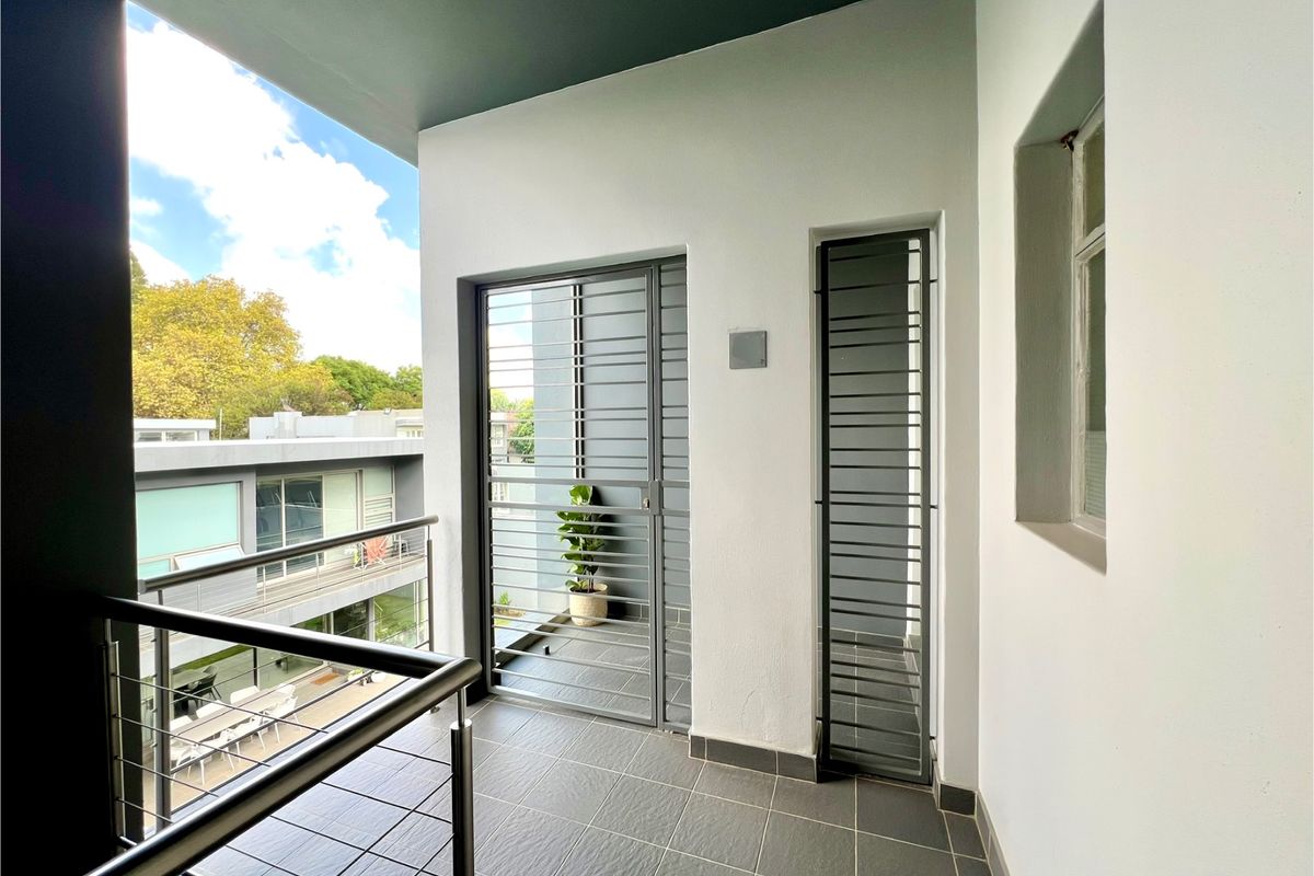 A modern, well-maintained balcony featuring tiled flooring, stainless steel balustrades, and secure metal gates, offering a clean outdoor space.