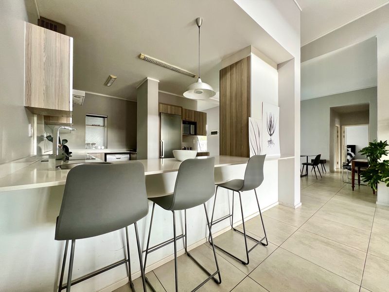 Modern open-plan kitchen featuring sleek cabinetry, stone countertops, and a breakfast bar, seamlessly flowing into the adjacent living and dining areas.