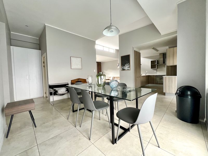 An open-plan living and dining area featuring neutral ceramic tile flooring, modern cabinetry, and a seamless transition to the kitchen space.