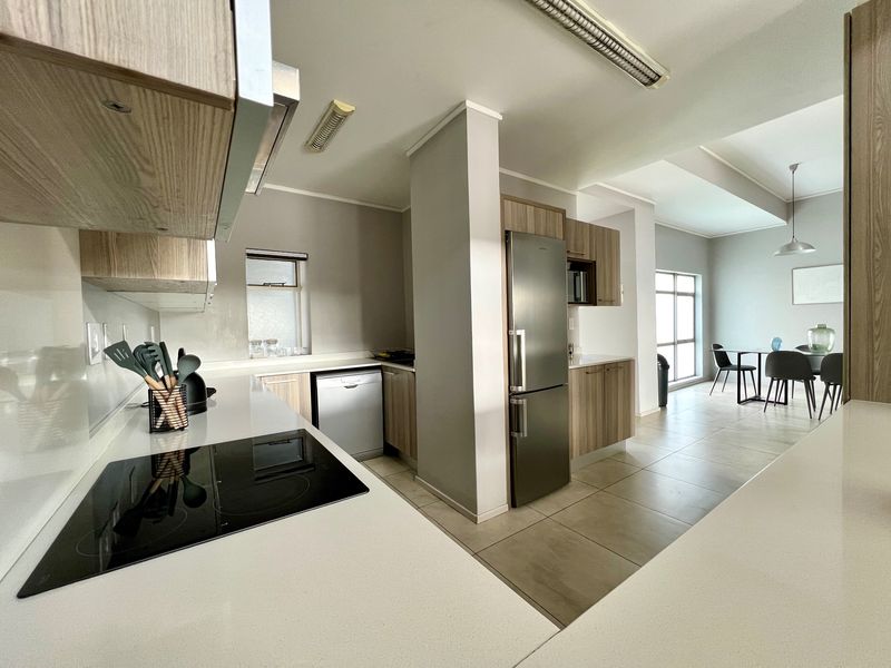 Modern open-plan kitchen and dining area featuring sleek cabinetry, stone countertops, integrated appliances, and neutral tiled flooring throughout.