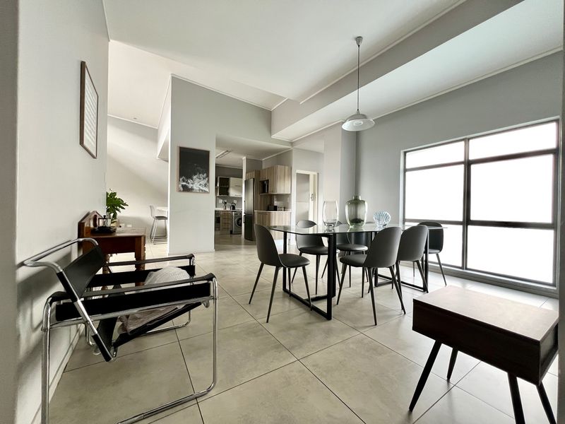 Spacious open-plan living and dining area featuring large windows, neutral tiled flooring, and a seamless flow into the adjacent kitchen space.