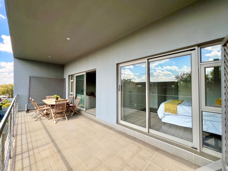 Spacious covered balcony featuring tiled flooring, modern sliding glass doors, and a metal balustrade, offering a seamless transition between indoor and outdoor living areas.