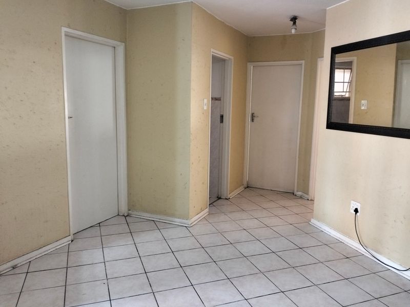A vacant hallway featuring tiled flooring and multiple internal doors, requiring cosmetic updates to the wall finishes.
