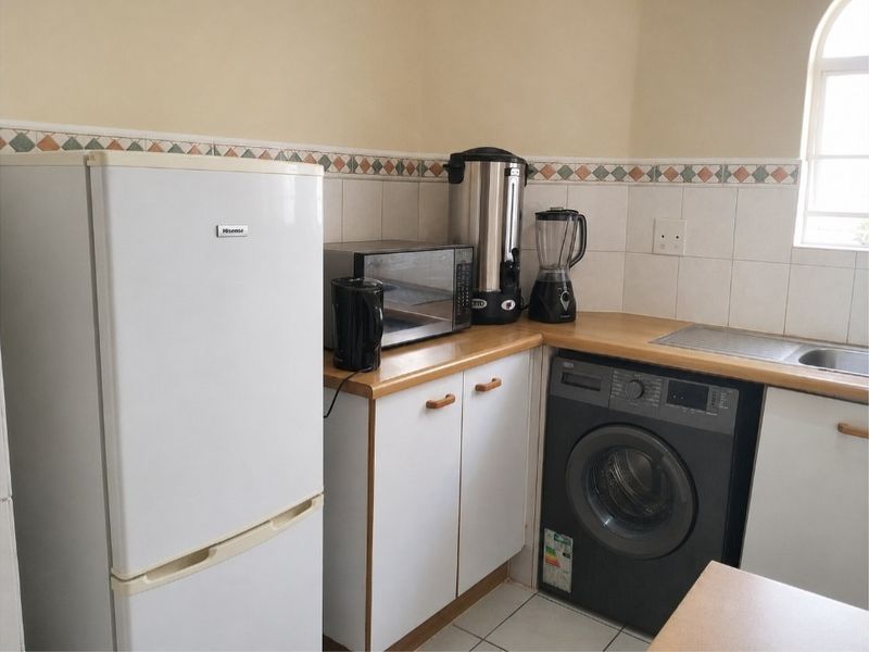A functional laundry area featuring laminate countertops, tiled backsplash, built-in cabinetry, and a stainless steel sink under an arched window.