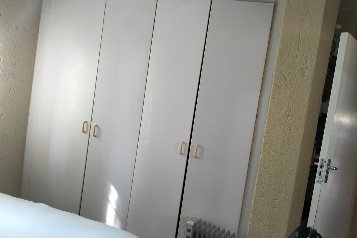 A bedroom featuring built-in white cupboards with textured wall finishes, requiring minor cosmetic updates to improve the overall aesthetic and finish quality.