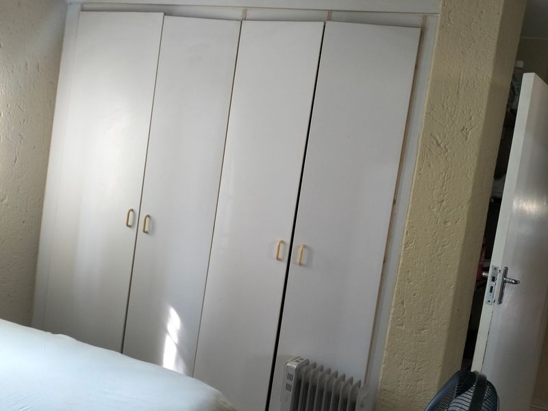 A bedroom featuring built-in white cupboards with textured wall finishes, requiring minor cosmetic updates to improve the overall aesthetic and finish quality.