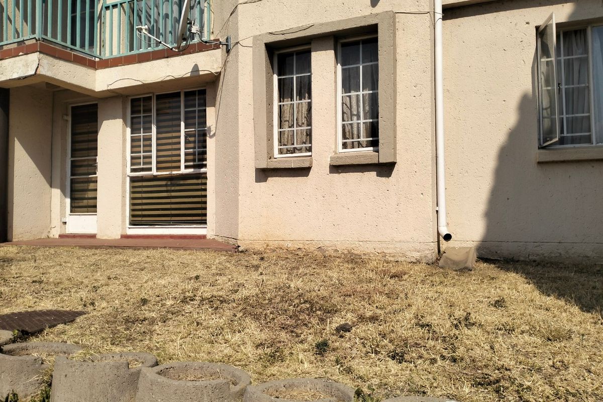Rear exterior view of the apartment building featuring a balcony, casement windows, and a small garden area with concrete edging.