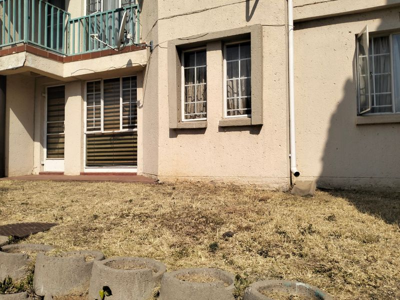 Rear exterior view of the apartment building featuring a balcony, casement windows, and a small garden area with concrete edging.