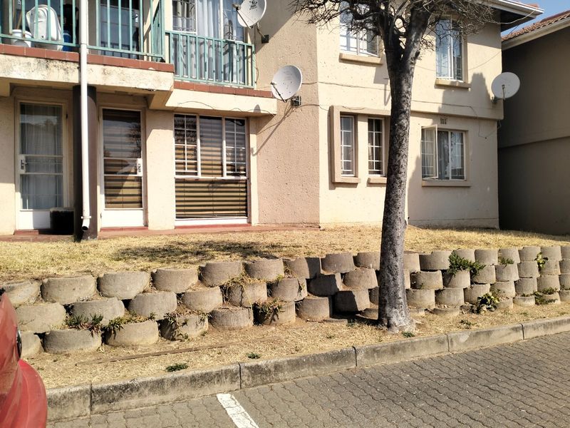 Front elevation of an apartment building featuring a concrete retaining wall, paved driveway, and balcony access.