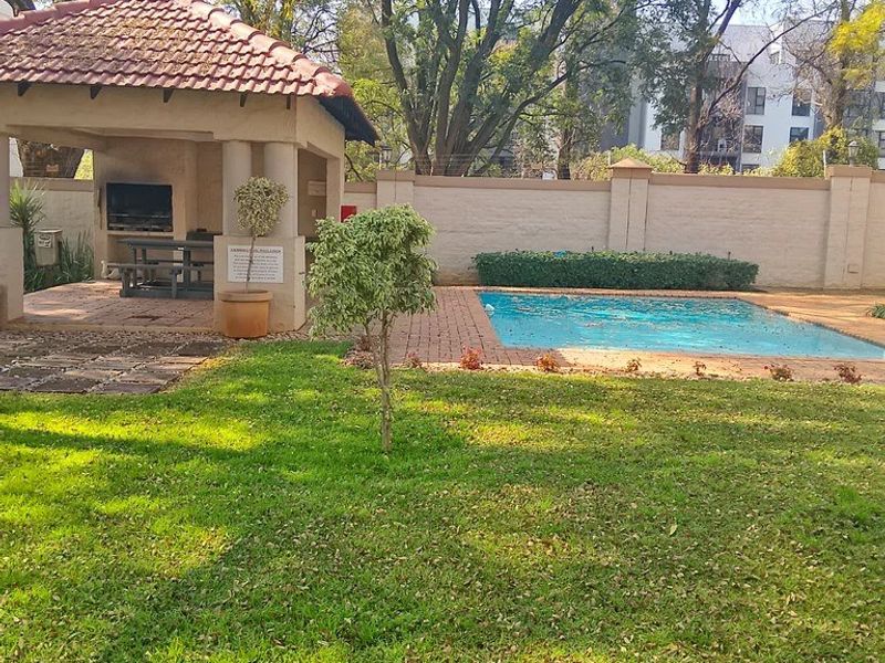 Outdoor communal area featuring a swimming pool, landscaped garden, and a covered lapa with a built-in braai facility.