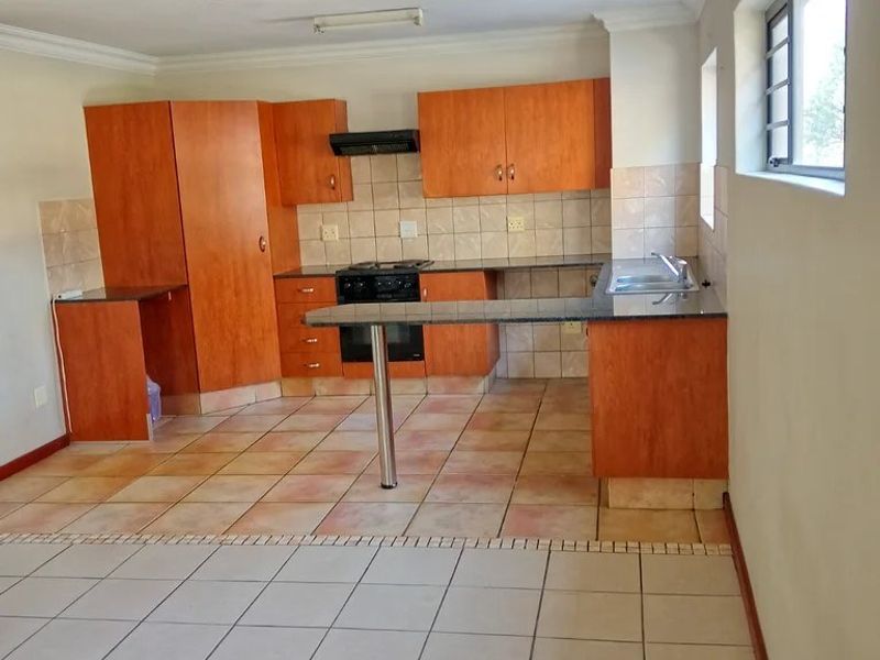 A functional kitchen featuring wooden cabinetry, granite countertops, a built-in oven with extractor fan, and tiled flooring throughout.