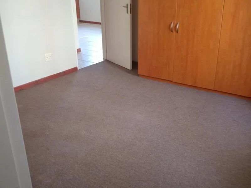 A vacant bedroom featuring built-in wooden cupboards and carpeted flooring, with a doorway leading to an adjacent room.