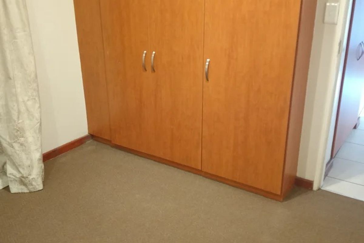 A bedroom featuring neutral carpet flooring and a built-in wooden wardrobe, offering a clean and functional space.