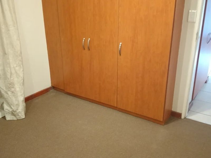 A bedroom featuring neutral carpet flooring and a built-in wooden wardrobe, offering a clean and functional space.