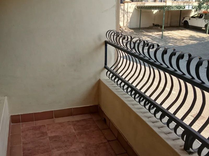 A compact balcony featuring tiled flooring and a decorative wrought iron balustrade, overlooking the complex parking area.