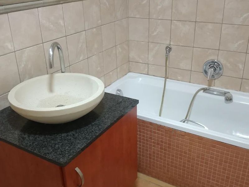 Bathroom featuring a vessel sink on a granite vanity, a built-in bathtub with mosaic tiling, and neutral ceramic wall and floor tiles.