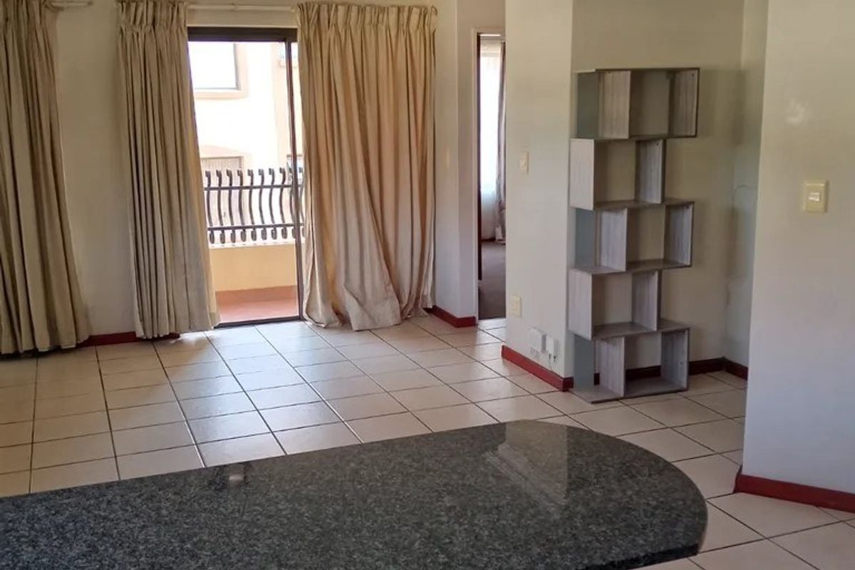 Open plan living area featuring ceramic tiled flooring, a granite breakfast bar, and direct access to a private balcony through sliding glass doors.